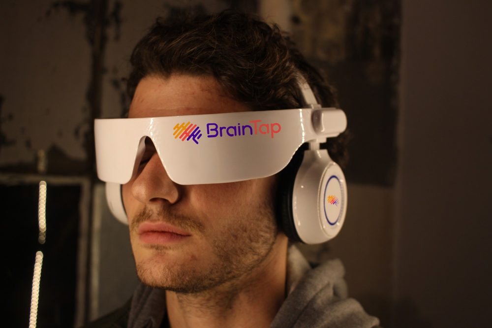 A man relaxes with his eyes closed wearing the BrainTap headset, with its light visor over his eyes and earphones on.