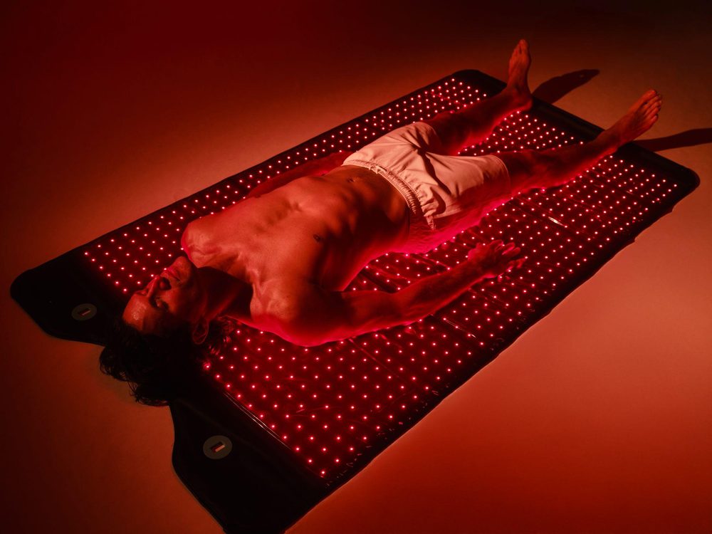 A man lies on the HigherDOSE Full Body Red Light Mat with its red LEDs lit.